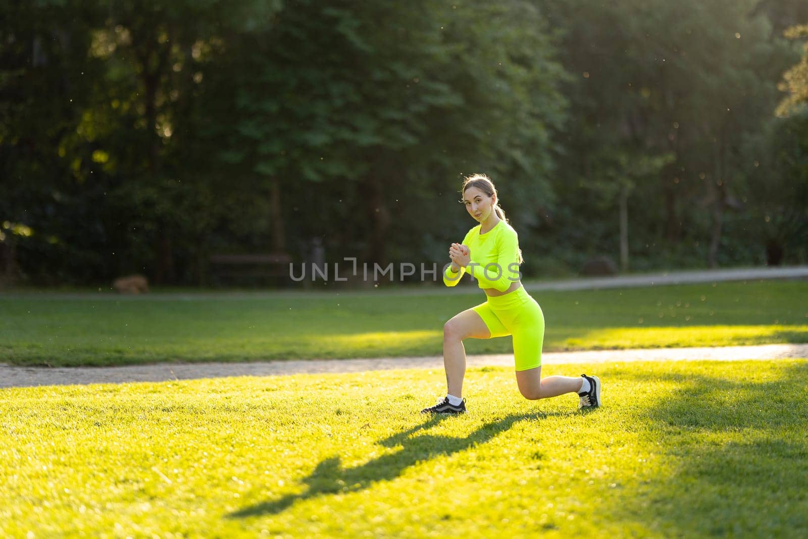 A woman in a neon green outfit is doing a yoga pose on a grassy field. The bright colors of her outfit and the lush green surroundings create a sense of energy and vitality