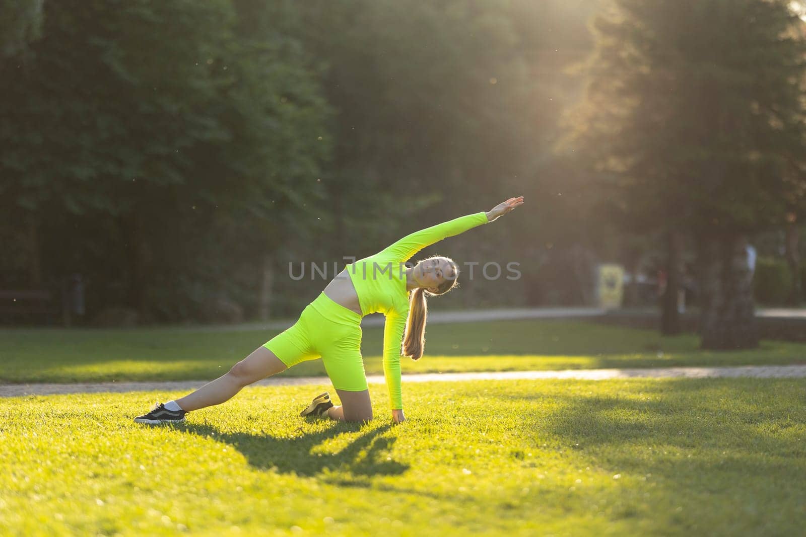 A woman in a neon green top and shorts is doing a yoga pose on a grassy field