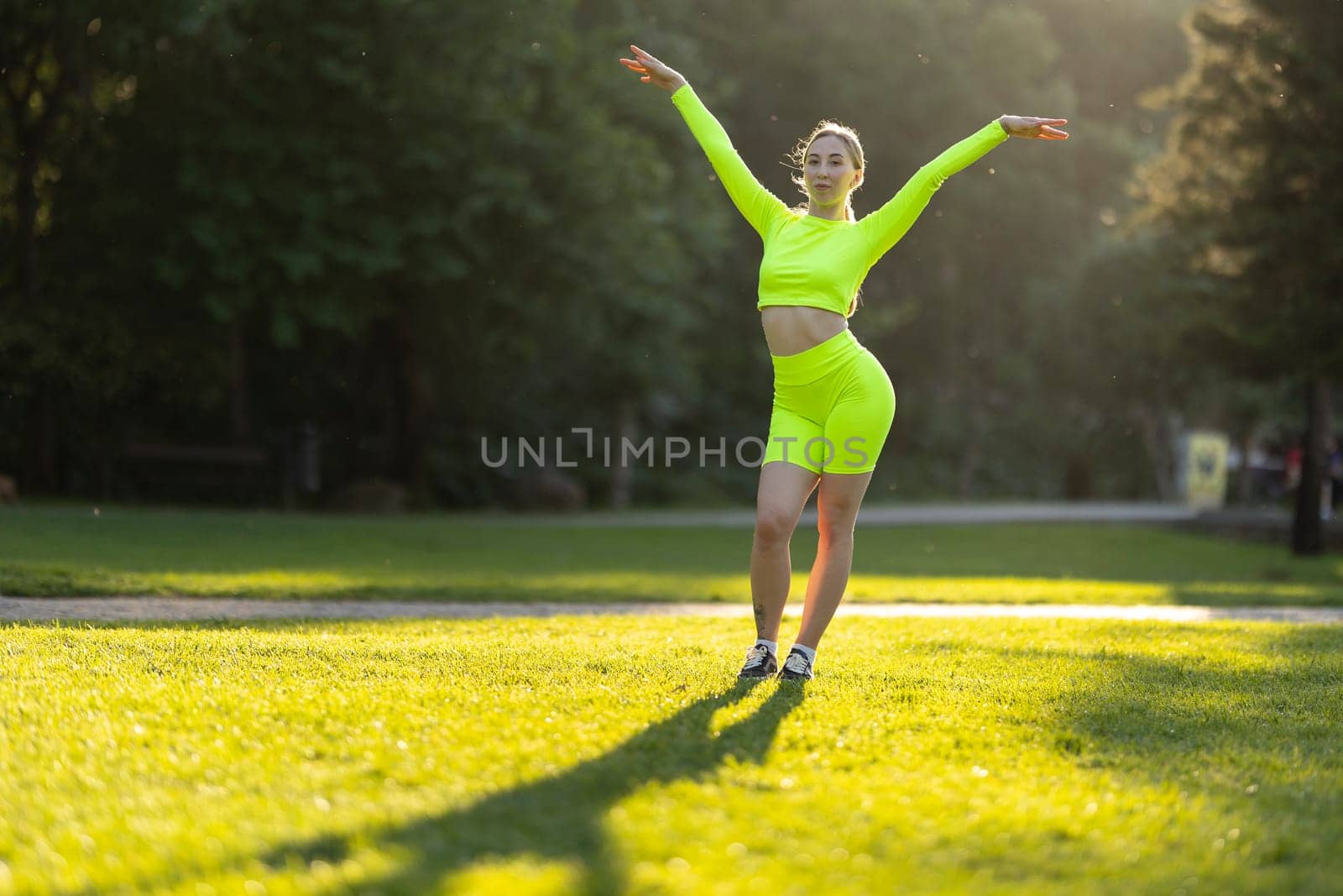 A woman in a neon green outfit is dancing on a grassy field by Studia72