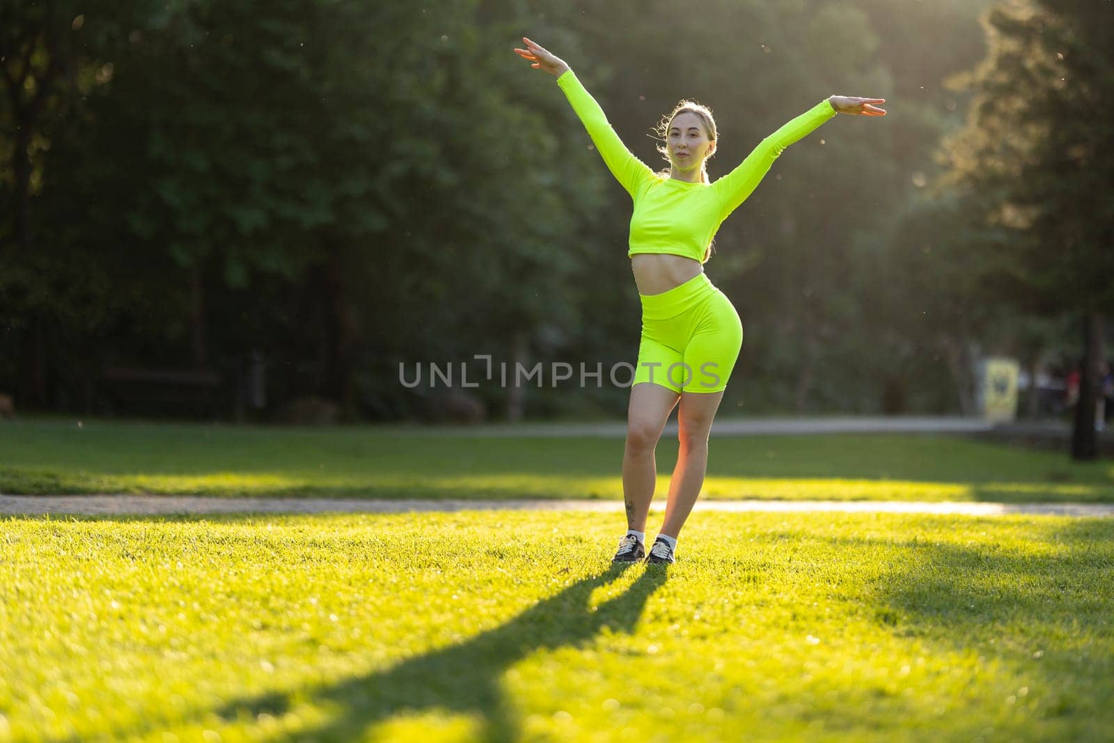 A woman in a neon green outfit is dancing on a grassy field. Concept of energy and joy, as the woman's vibrant outfit and her pose suggest that she is enjoying herself