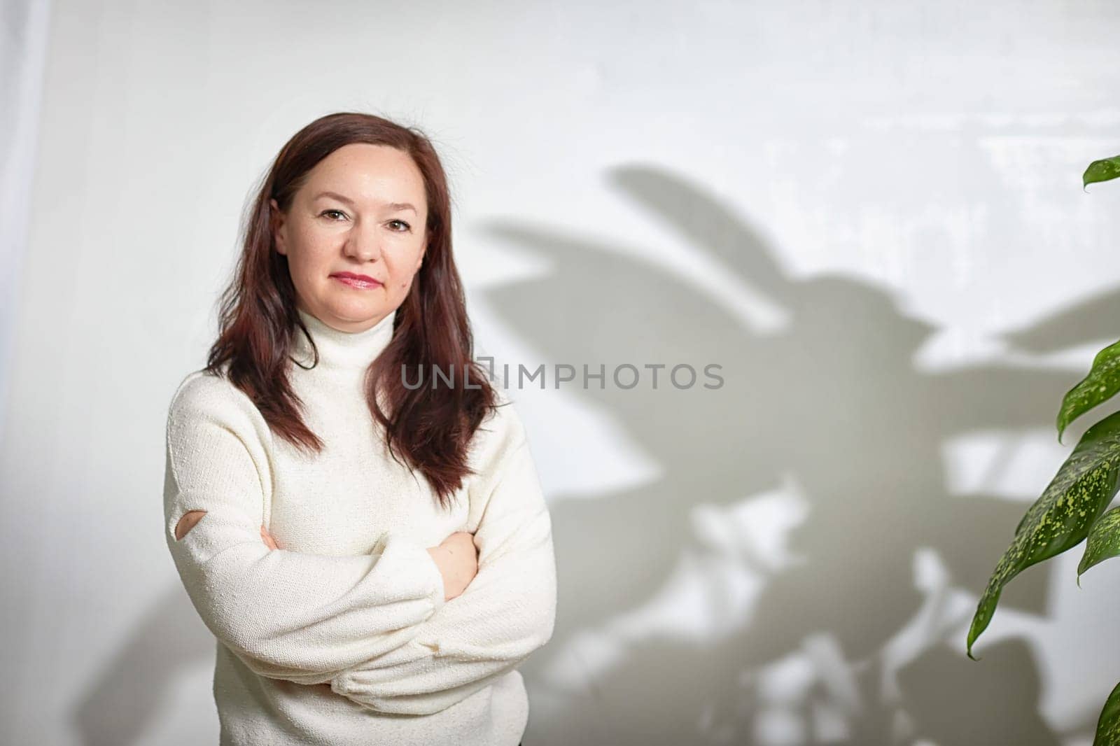 Portrait of Confident middle aged Woman Indoors Near Lush Green Plant. Mature woman posing in well-lit room