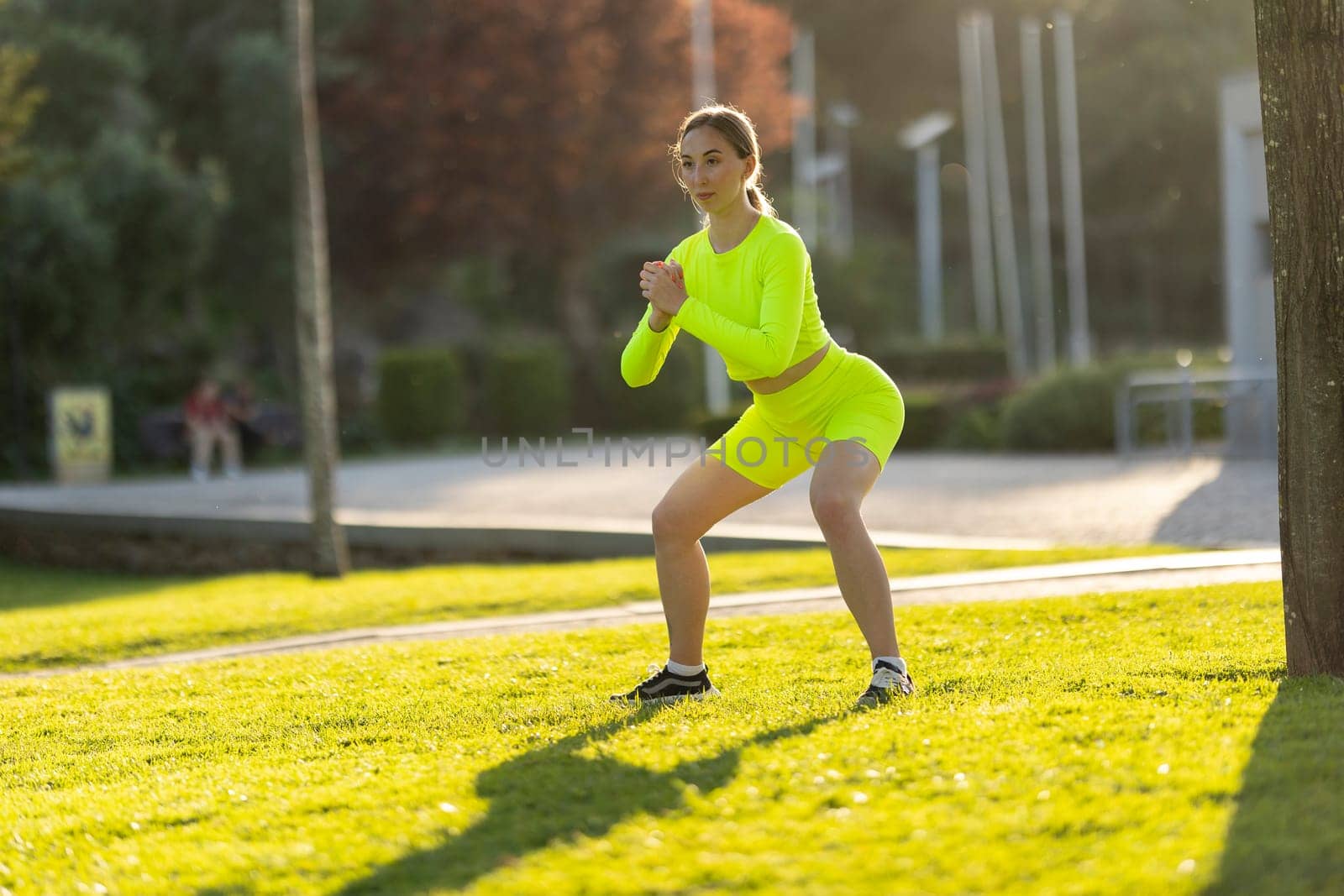 A woman in a neon yellow outfit is doing a yoga pose on a grassy field. The bright colors of her outfit and the green grass create a cheerful and energetic atmosphere