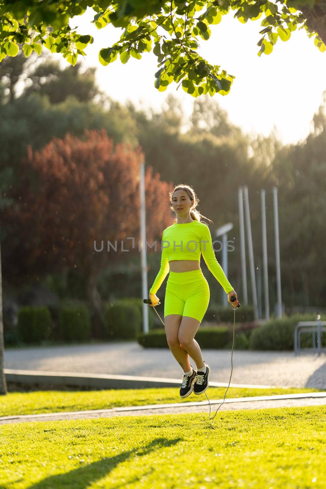 A woman in a neon yellow outfit is jumping rope in a park by Studia72