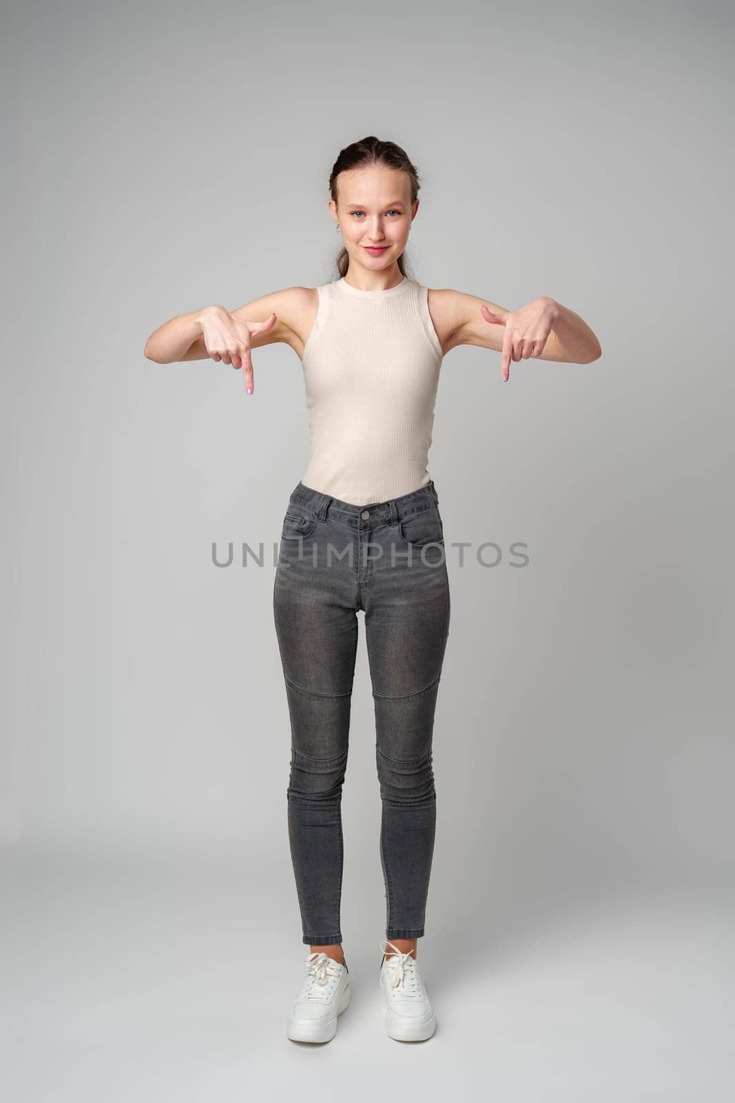 Young Woman in Tank Top Pointing Down in studio copy space