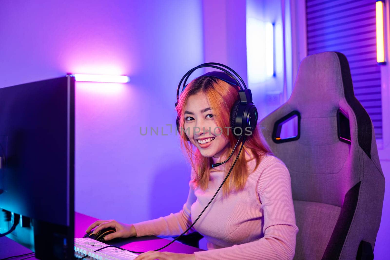 Happy Gamer endeavor plays online video games tournament with computer neon light, Smiling young woman wearing gaming headphones intend to do playing live stream games online at home looking to camera