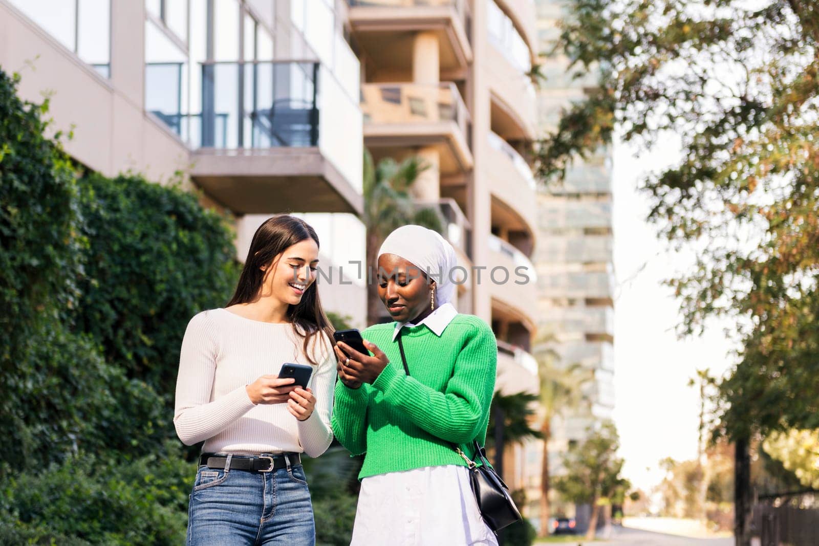 two young women walking down a street looking their cell phones, concept of friendship and technology, copy space for text