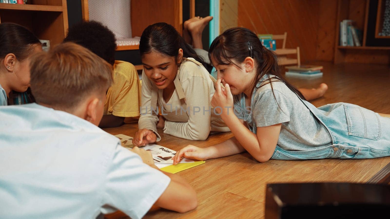 Caucasian smart girl listening young highschool boy talking about book at modern library. Group of student with mixed races reading picture book while lying down on floor in a circle. Edification.