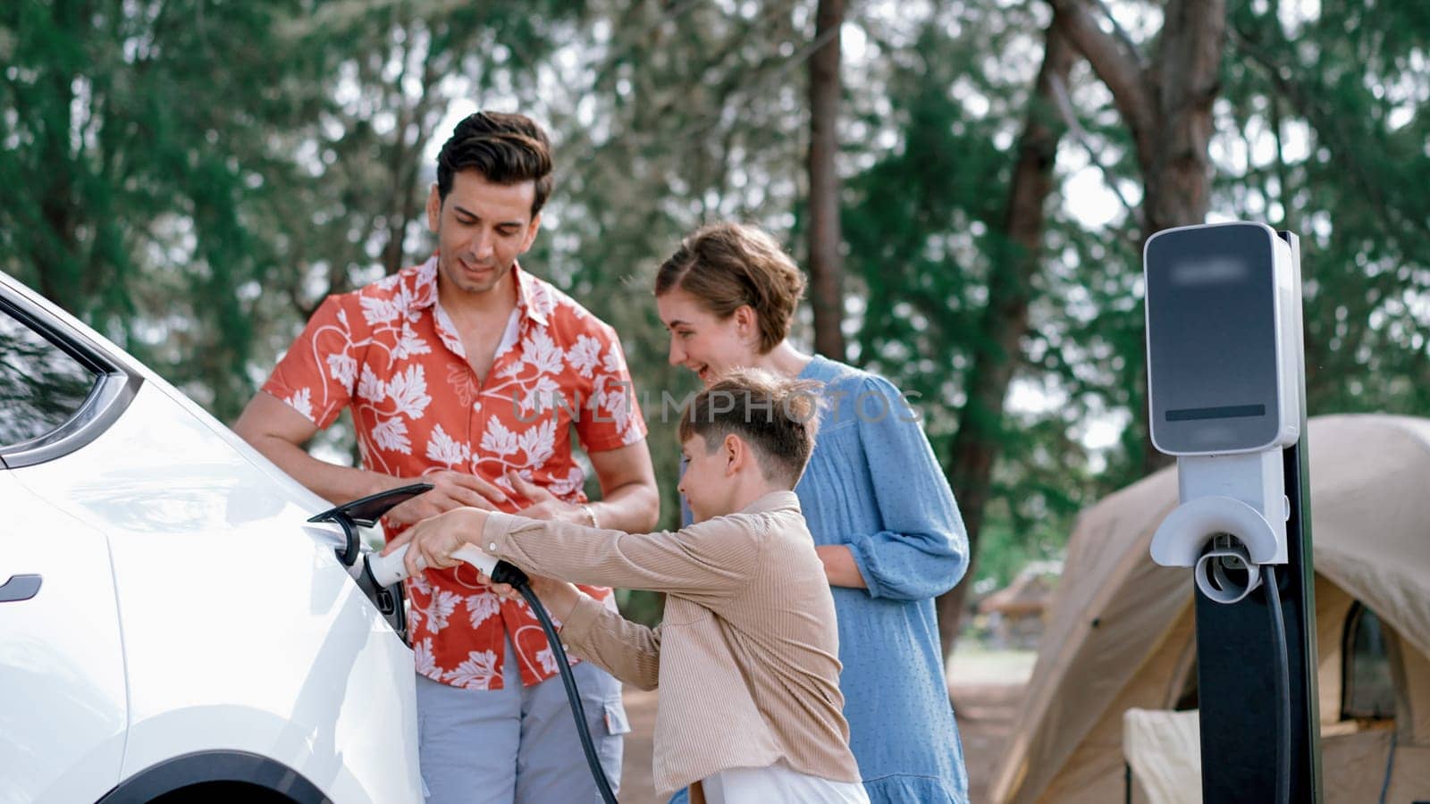 Outdoor adventure and family vacation camping in nature travel by eco friendly car for sustainable future. Lovely family recharge EV car with EV charging station in campsite. Perpetual