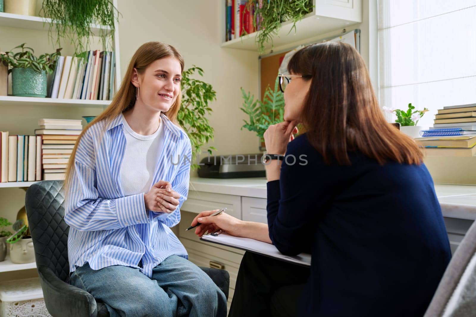 Smiling positive young teen female patient talking to professional mental therapist. Teenager girl high school college student in therapy with psychologist psychotherapist counselor. Treatment support