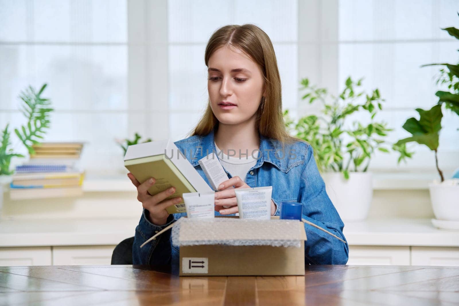 Young female customer sitting at home unpacking cardboard box with online purchases by VH-studio