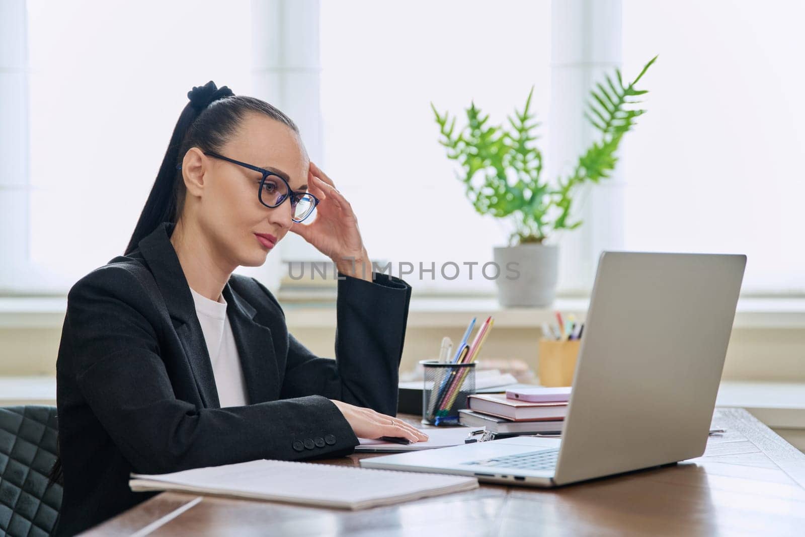 Business woman working in home office at desk with laptop computer. Serious 30s female typing and looking at monitor. Remote business, technologies internet, teaching, blogging, work freelance concept