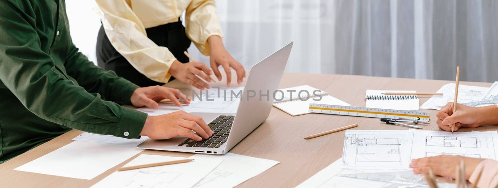 Professional architect edited blueprint by using laptop while project manager point the mistake point at meeting room on meeting table with architectural document scatter around. Closeup. Delineation.
