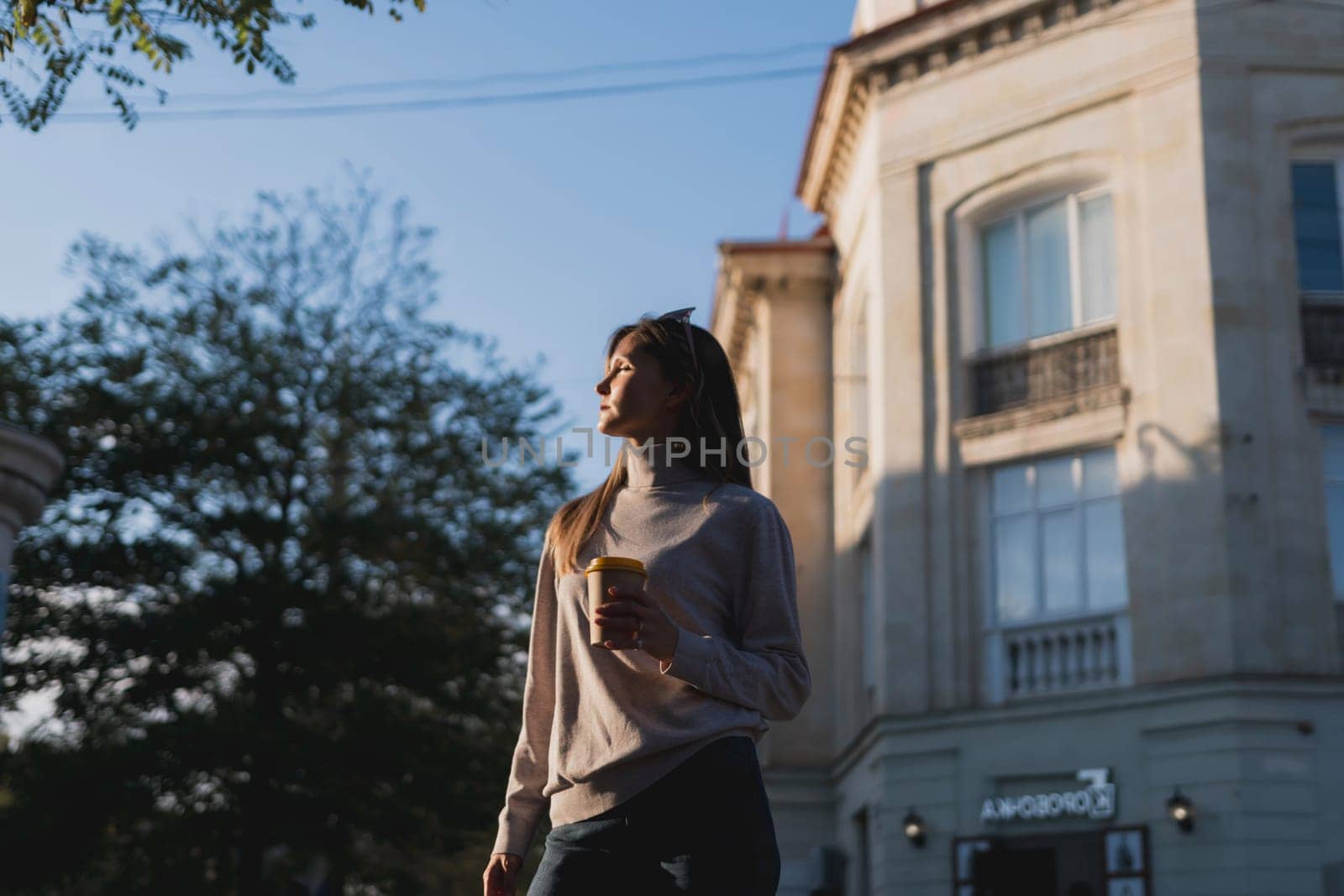 A woman is walking down the street holding a cup of coffee. The image has a calm and peaceful mood, as the woman is walking alone and enjoying her coffee. by Matiunina