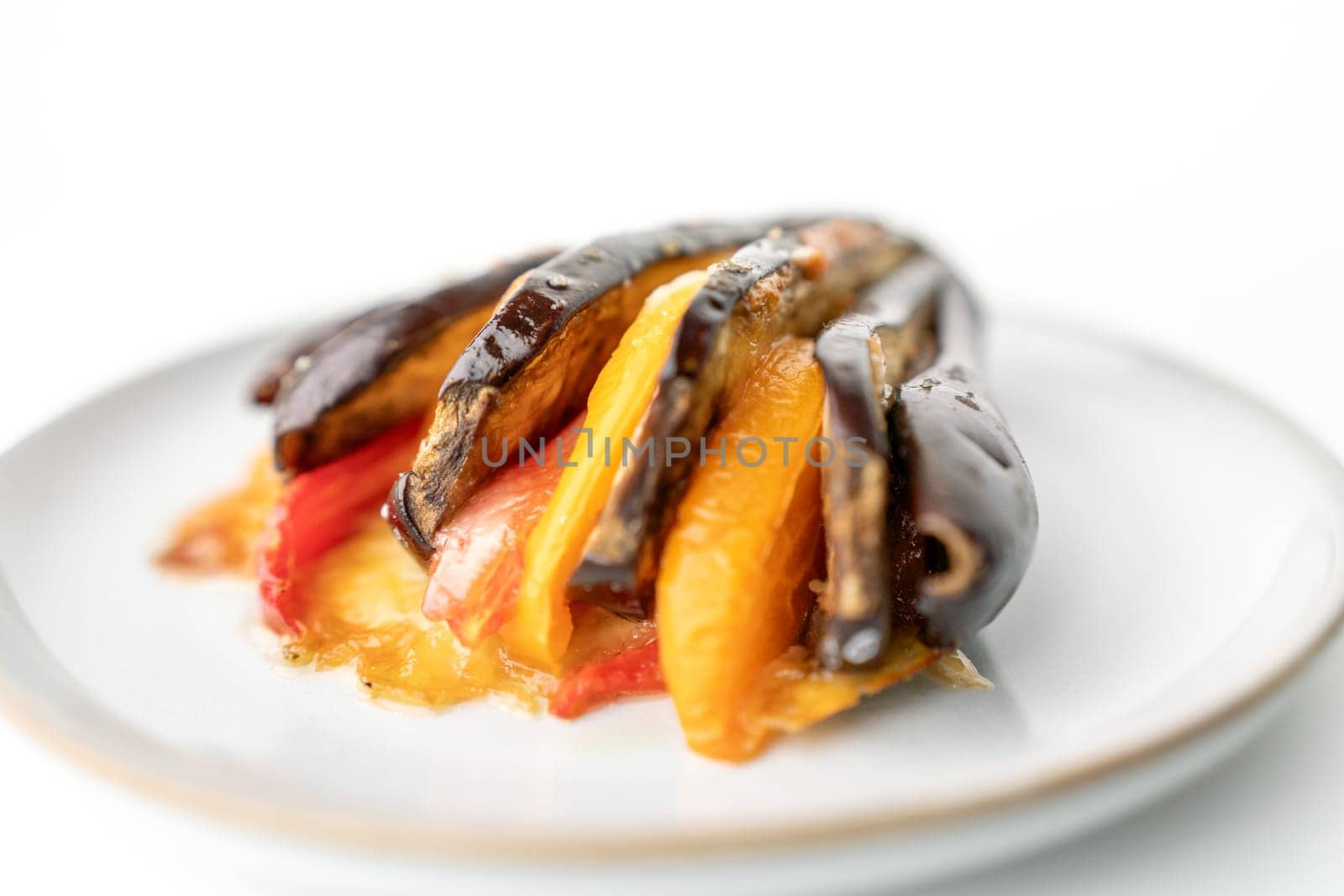 A plate of food with a variety of vegetables, including peppers and eggplant. The dish is served on a white plate and he is a healthy and colorful meal. by Matiunina