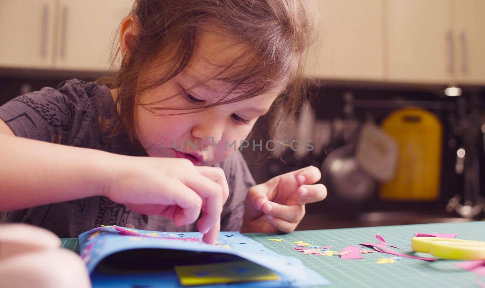 Scrapbooking. Little girl doing a postcard. She is glueing colored paper. Children's creativity, handicraft