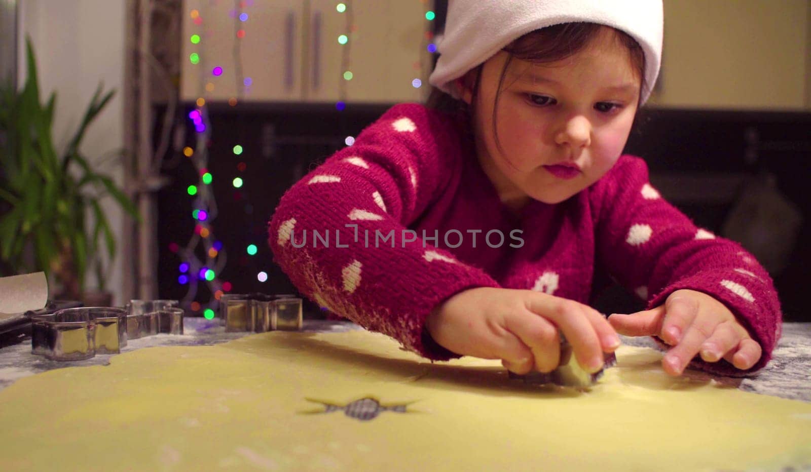 Little girl in red sweater carves Christmas cookies by Chudakov