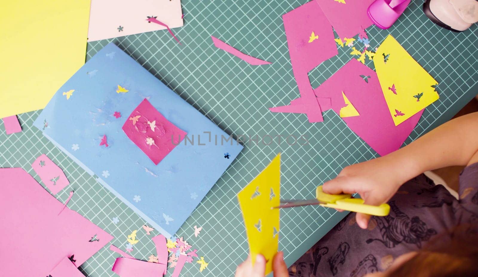 Top view. Scrapbooking. Hands of little girl cutting colored paper with scissors. Children's creativity, handicraft