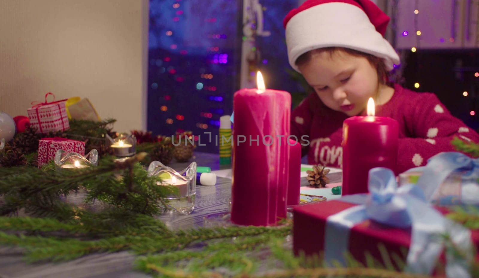 Children handicraft. Little girl glues New Year card. Table with Christmas decorations. French text on a sweater - falls