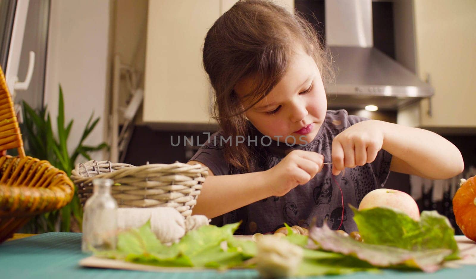 Autumn. Little girl sitting at the desk makes necklace of acorns