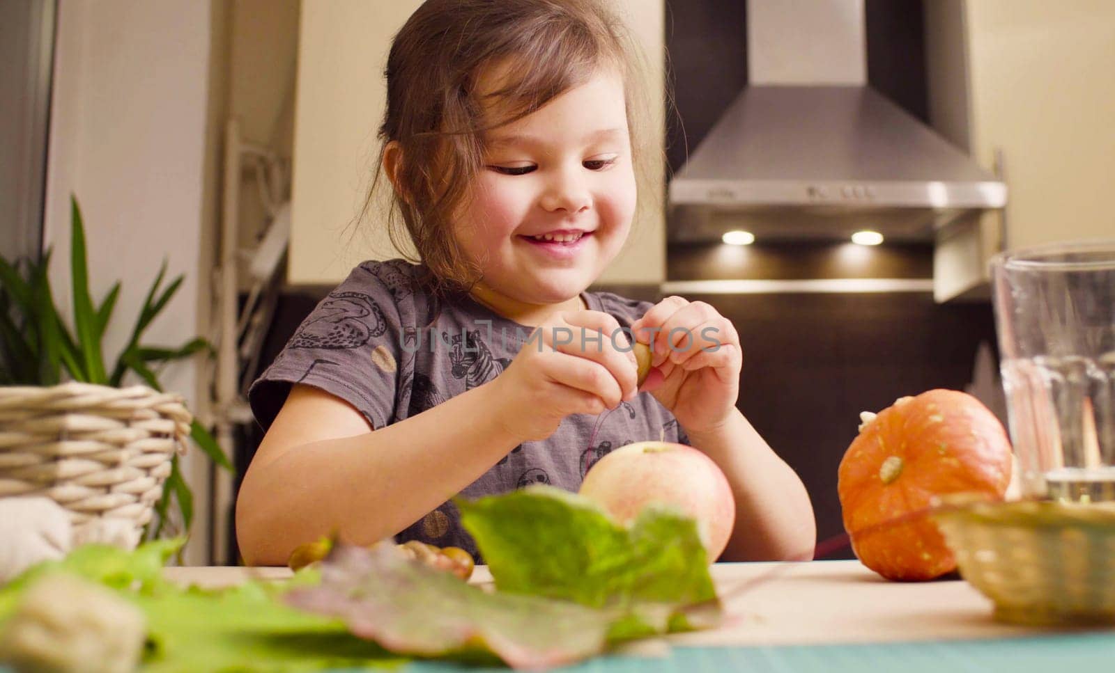 Autumn. Little girl sitting at the desk makes necklace of acorns