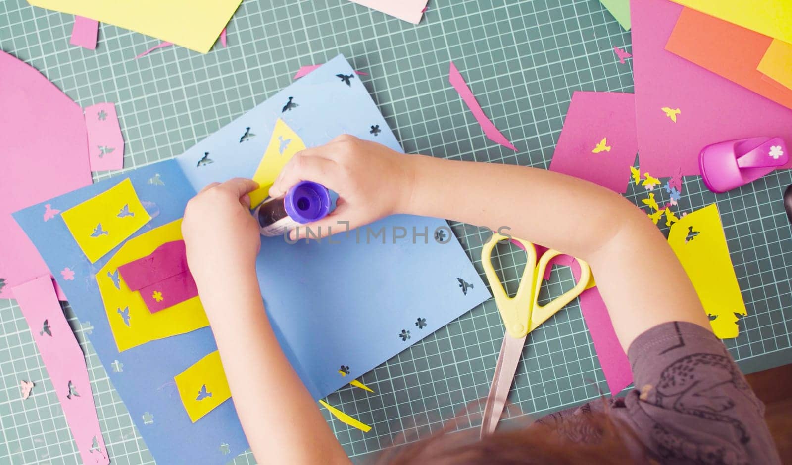 Top view. Scrapbooking. Hands of little girl gluing colored paper. Children's creativity, handicraft