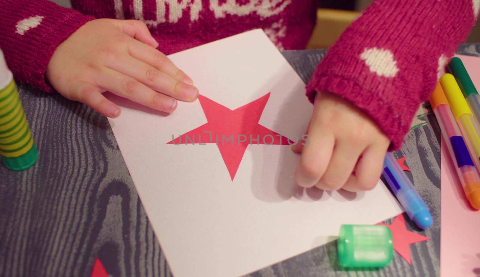 Top view. Close up. Little girl glues New Year card. Table with Christmas decorations.