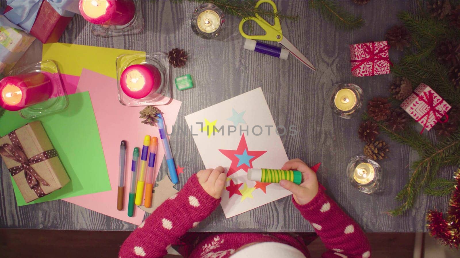 Top view. Little girl glues New Year card. Table with Christmas decorations.