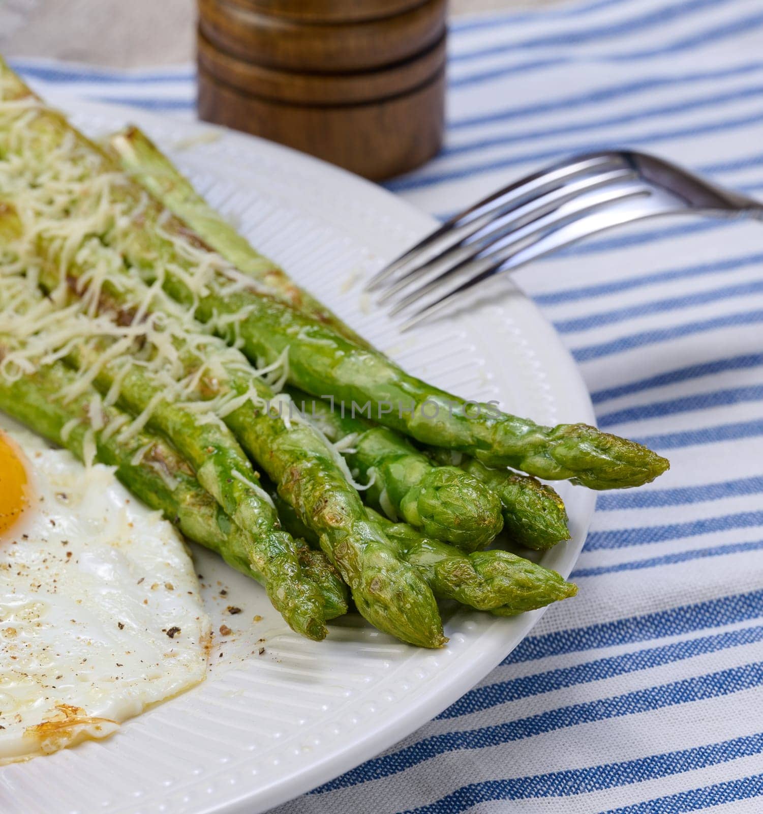 Cooked green asparagus stalks and sprinkled with grated cheese in a white plate by ndanko