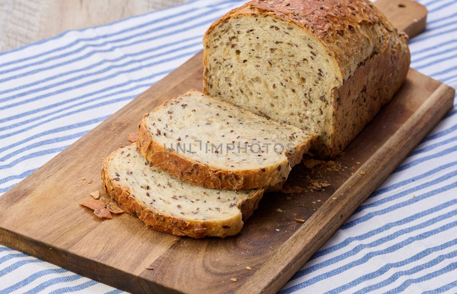 Sliced ​​white wheat flour bread with flax seeds on a wooden board by ndanko