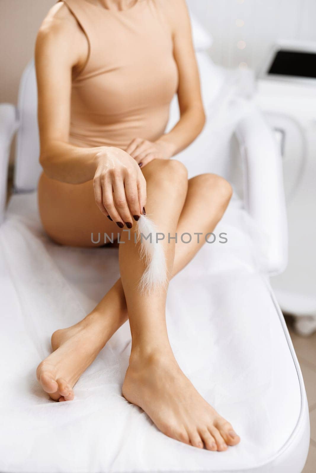 Young Woman's Hand Touching Her Legs With White Feather. Female feet with smooth skin and soft feather. Beautiful Body Care Concepts by uflypro