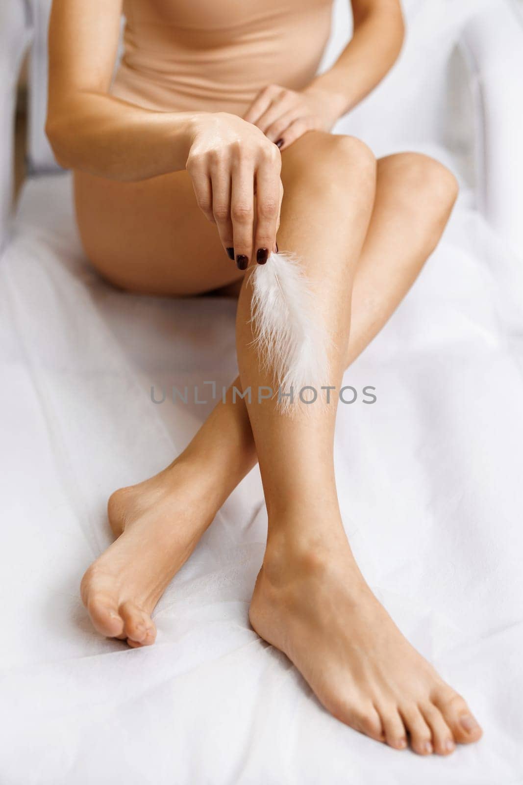 Closeup of female legs with smooth skin and soft ostrich feather. Concepts of skin care and hair removal treatment. Woman touches her legs with white feather.