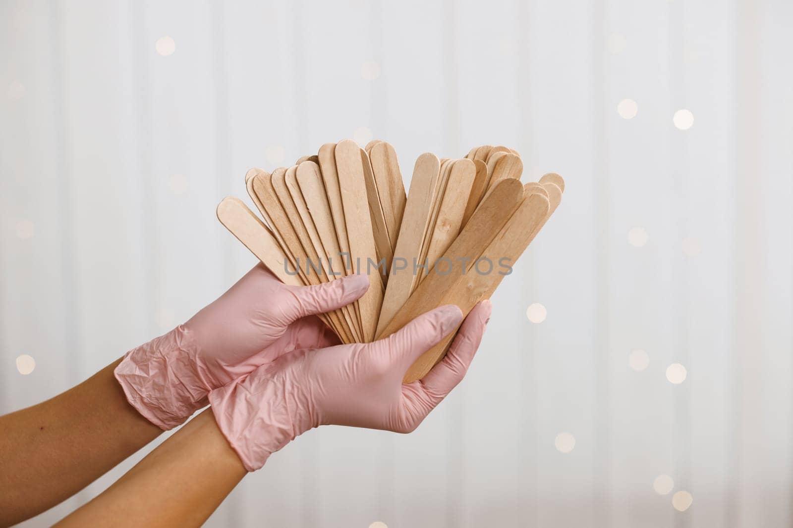 Woman holding many wax wooden spatulas. The young woman is wearing beige clothing and in pink medical gloves. The concept of beauty, depilation, waxing, sugaring smooth skin without hair, banner