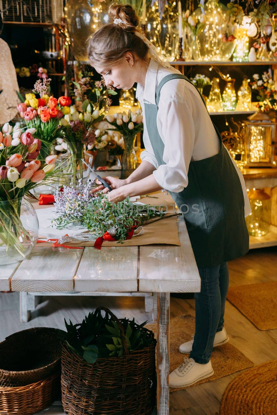 A woman in her florist shop collects bouquets of flowers. The concept of a small business. Bouquets of tulips for the holiday on March 8. by Annu1tochka