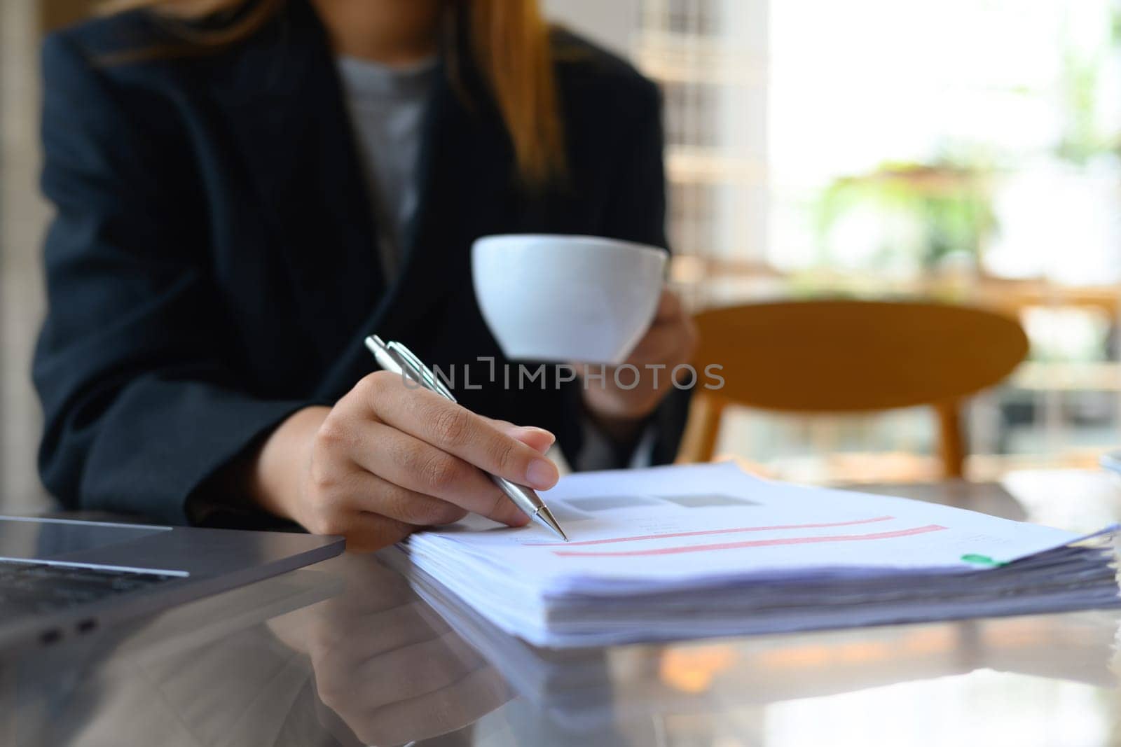 Businesswoman doing some paperwork and drinking coffee at office desk by prathanchorruangsak