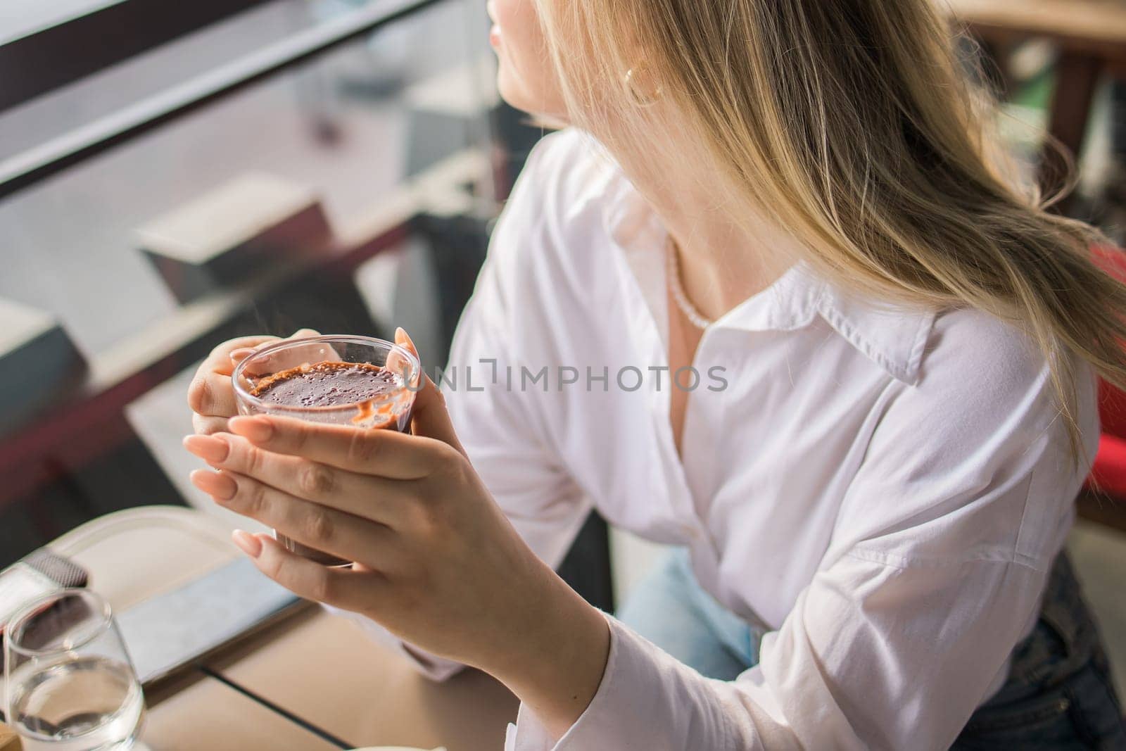 Gen z blonde woman drinks hot chocolate in summer cafe. Tasty beverage and break concept. Generation z people by Satura86
