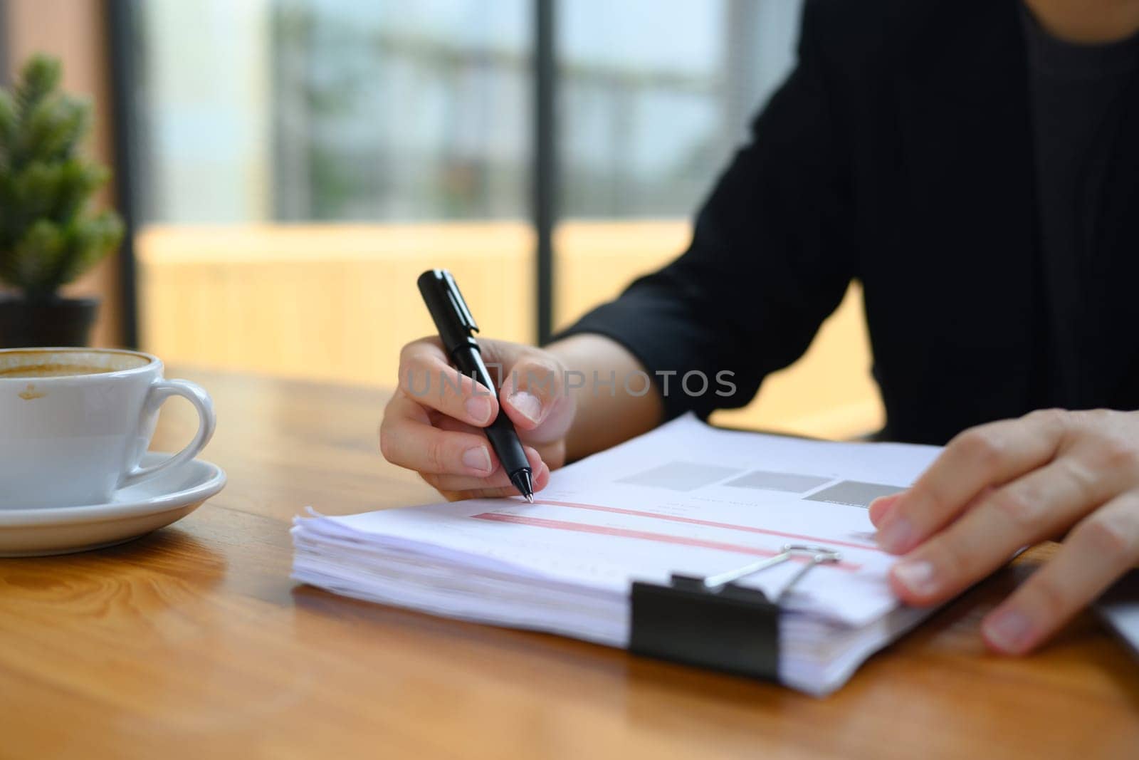 Cropped shot accountant in black suit working with financial reports on wooden desk.