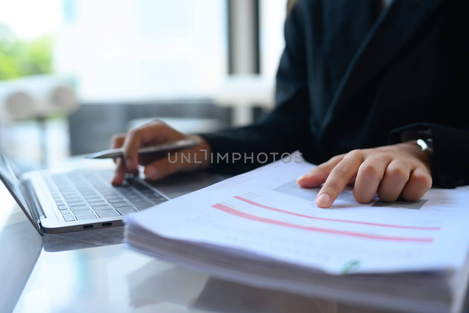 Female accountant working with financial reports and using laptop at desk.