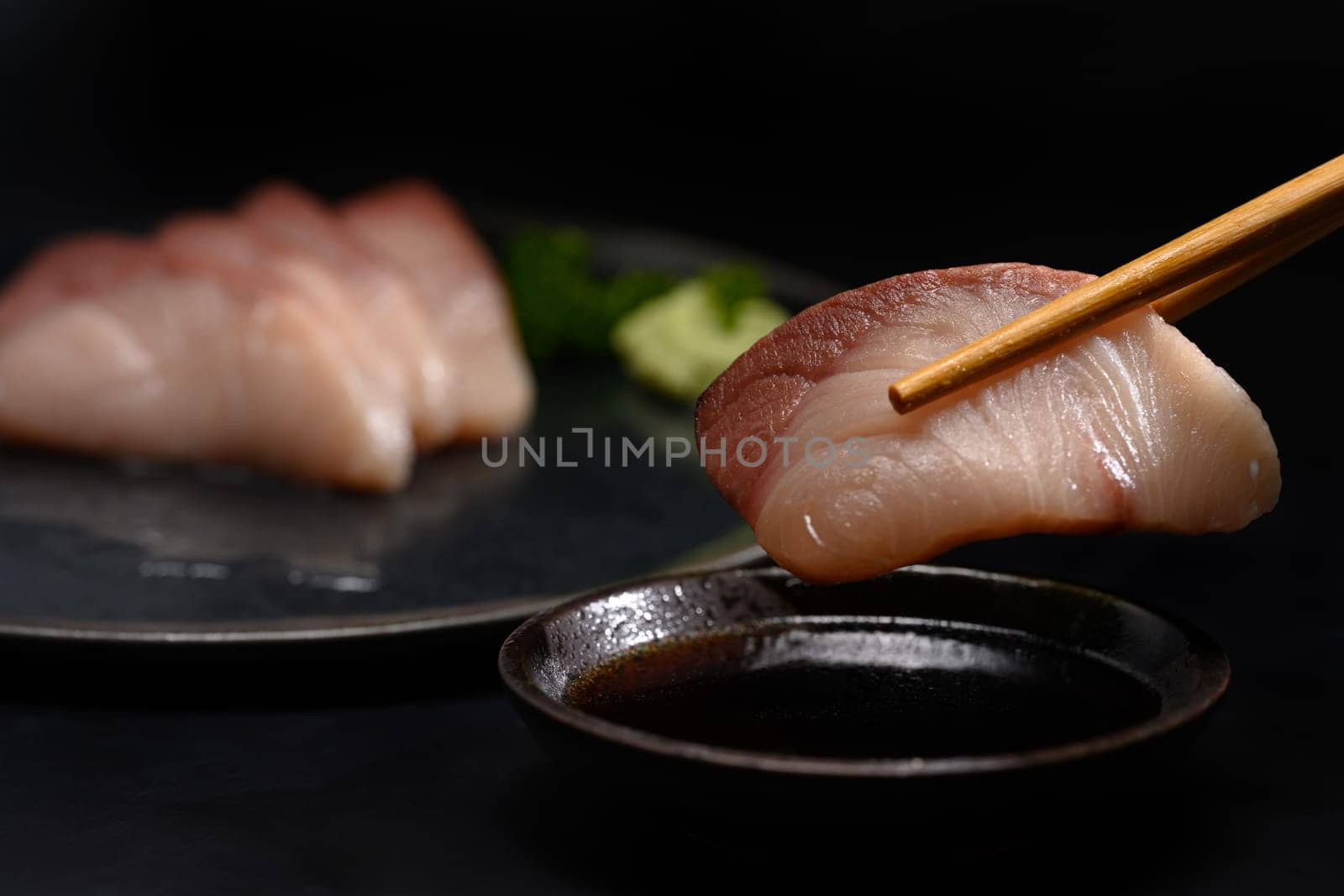 Closeup chopsticks with Yellow tail fish or Hamachi Sashimi dipping into soy sauce.