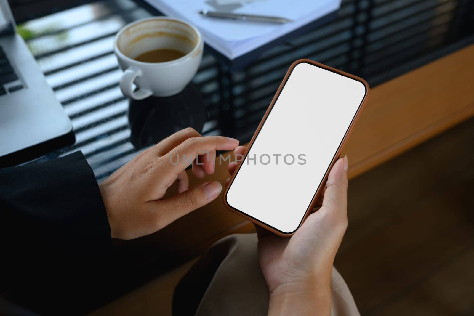 Businesswoman holding mobile phone with empty screen sitting at office desk.