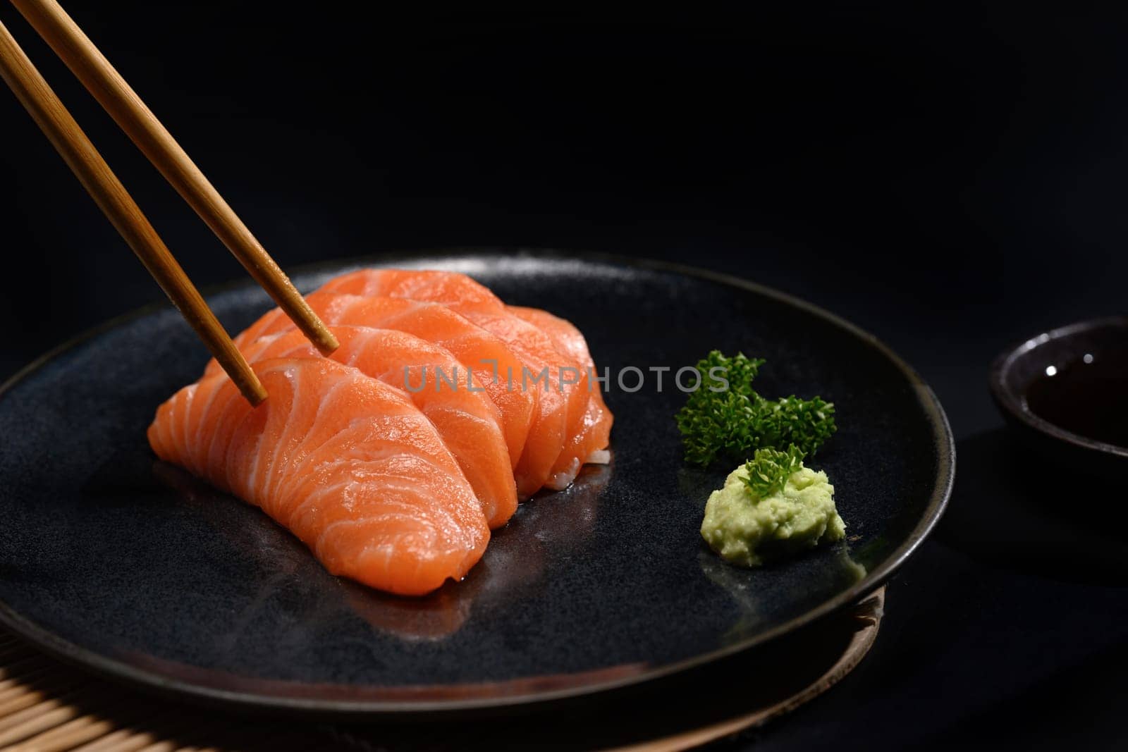 Fresh salmon sashimi on black plate with wasabi and parsley leaf. Japanese food style by prathanchorruangsak