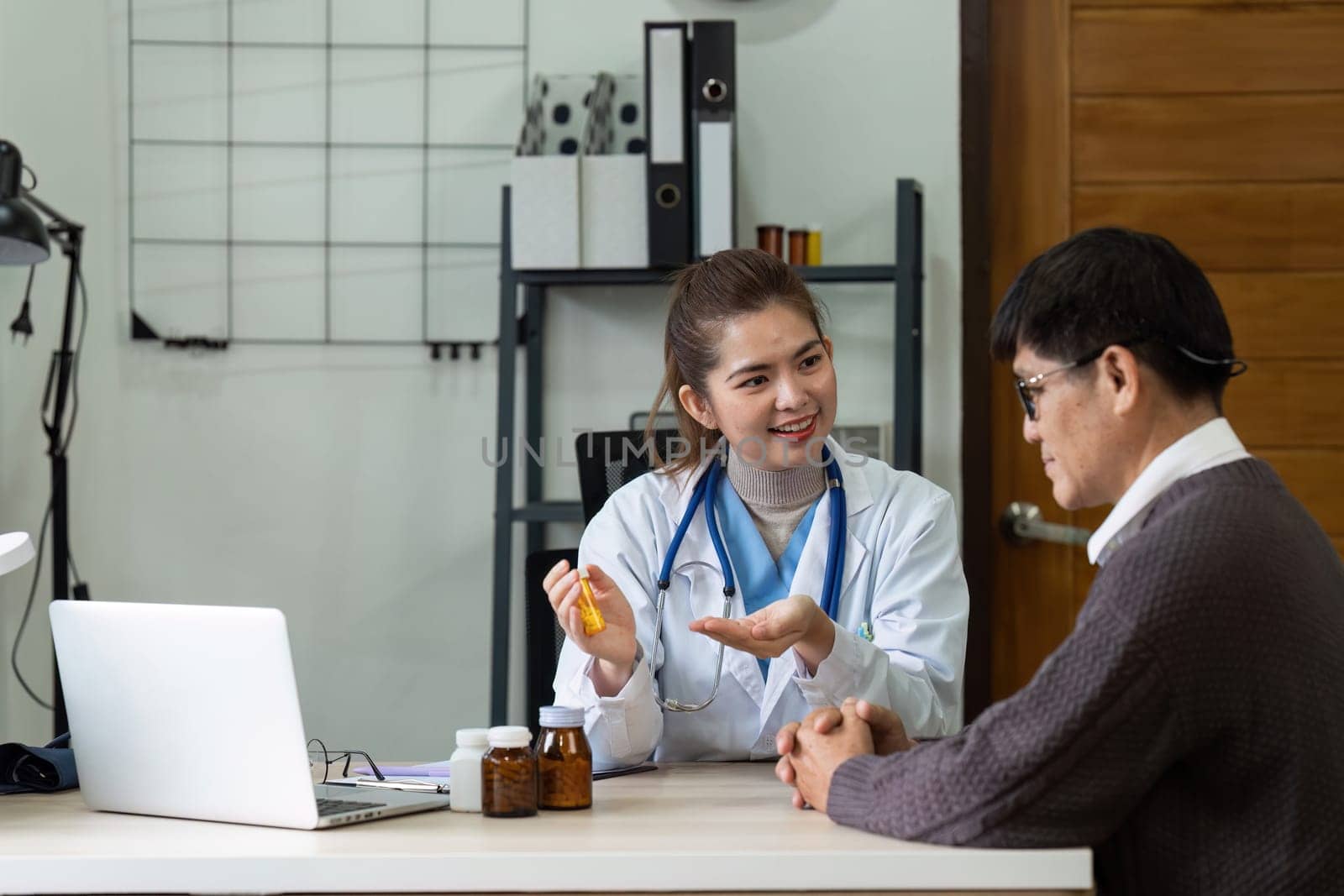 A woman doctor is talking to a man in a room. The woman is holding a bottle of pills and the man is sitting on a chair