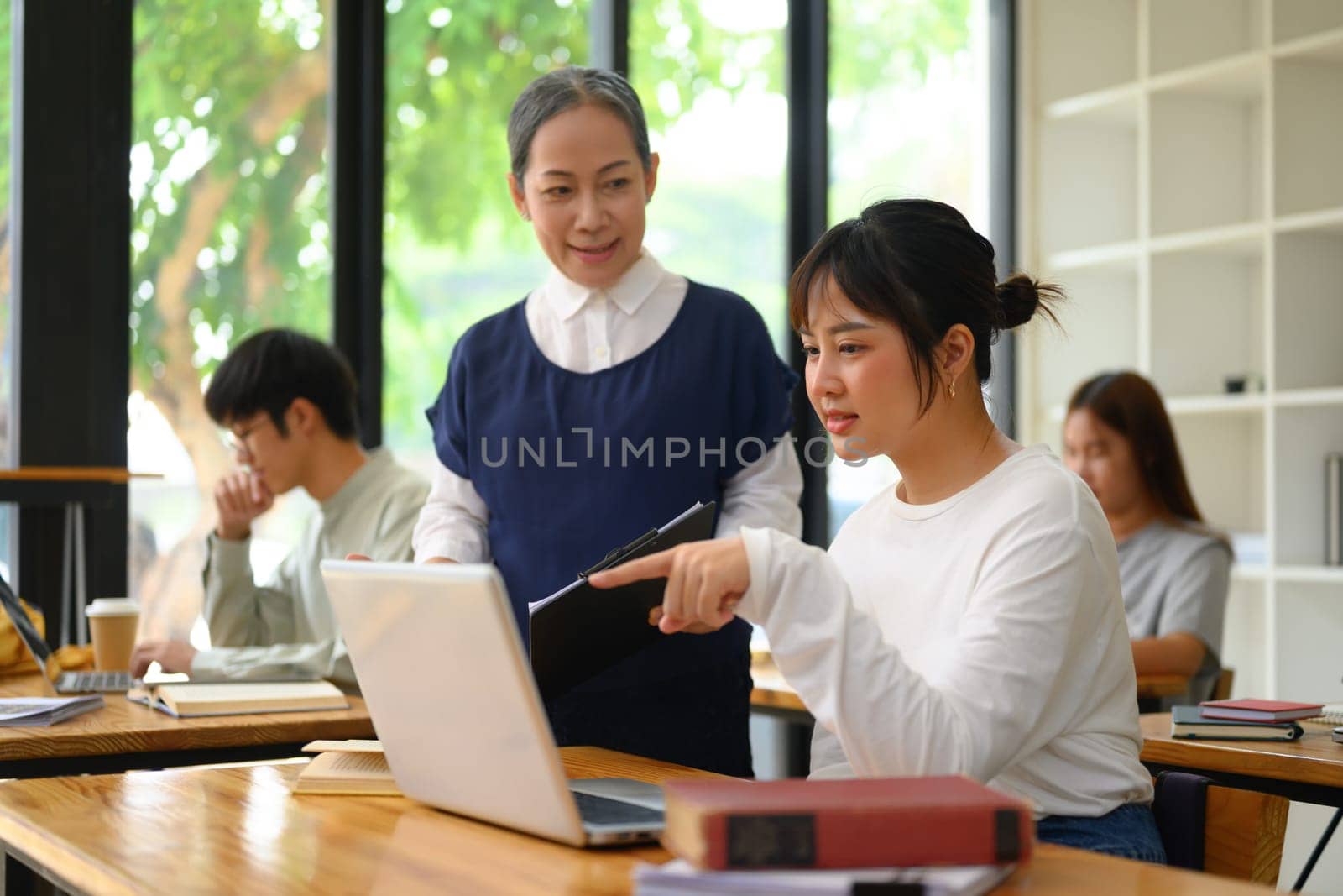 Friendly senior professor helping female student with assignment.