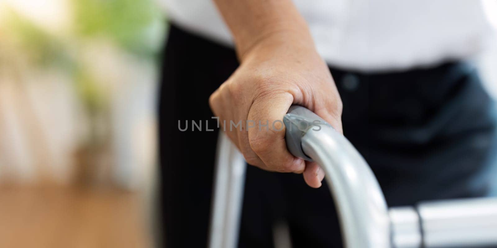A person is holding a walker with a hand on the handle. The person is wearing a white shirt and black pants