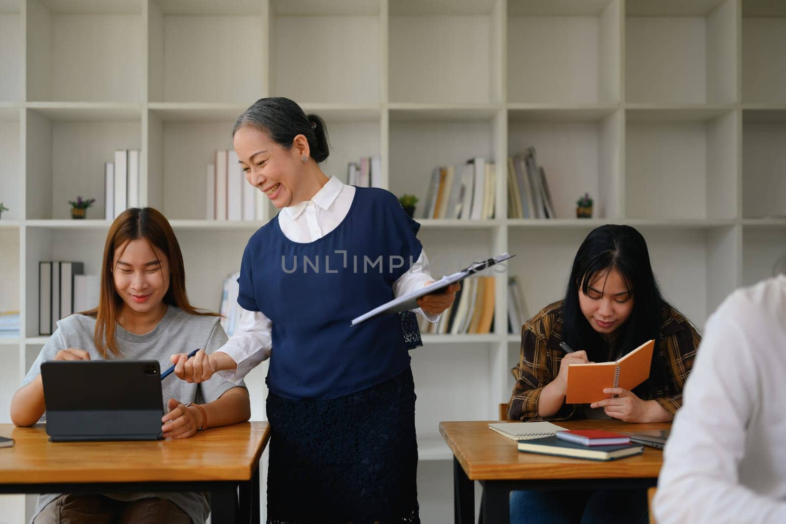 Smiling middle age lecturer explaining something to student woman during her class by prathanchorruangsak