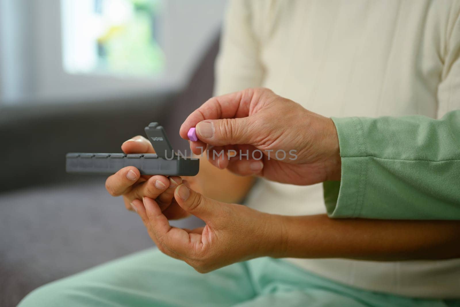 Closeup mature man taking prescription medicine on couch at home. Healthcare and medication concept.