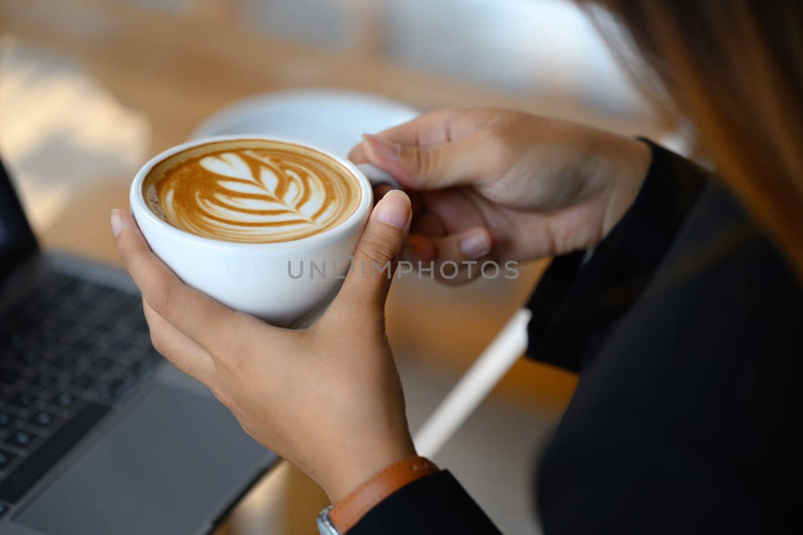 Close up shot of female hands holding cup of coffee with beautiful latte art by prathanchorruangsak