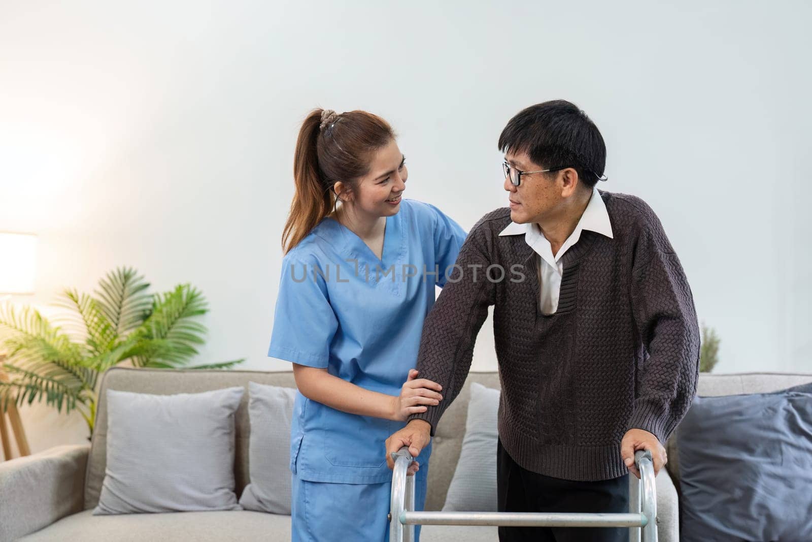 Nurse or caregiver help elderly walk by using walker at home. healthcare home visit concept by itchaznong