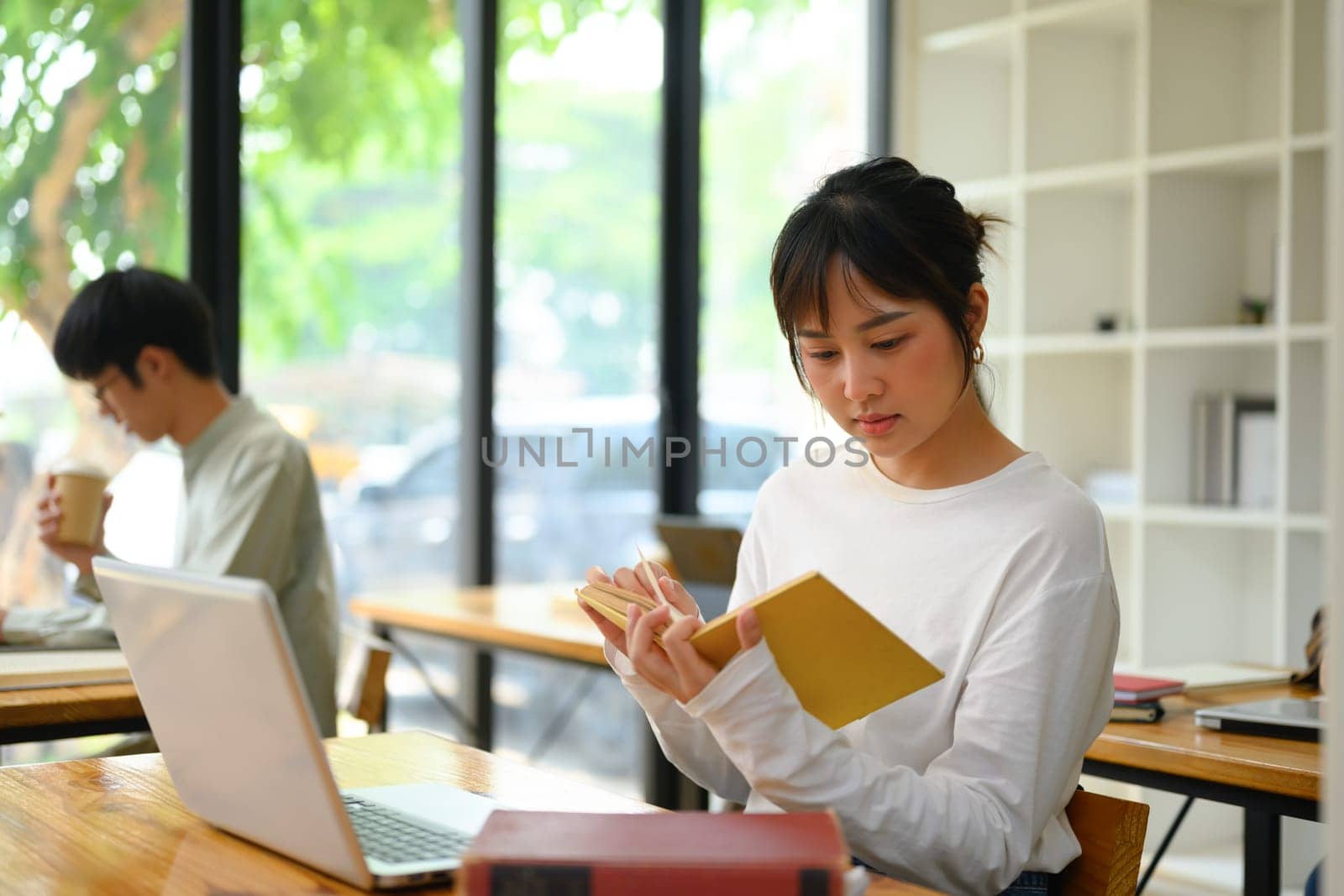 Back view of a female student using laptop during class at university in library by prathanchorruangsak