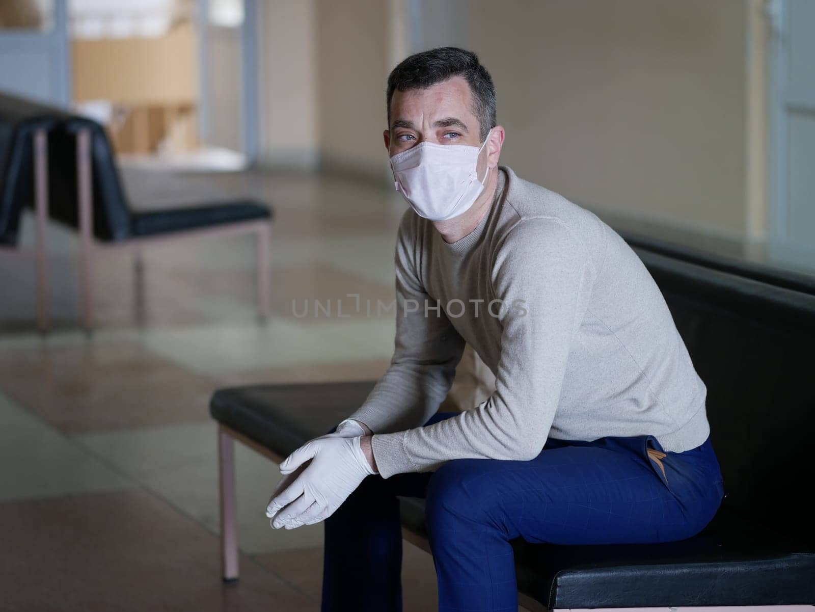 Man wearing protective gloves on hands and mask on face nervously impatiently waiting in the lobby in covid 19 virus