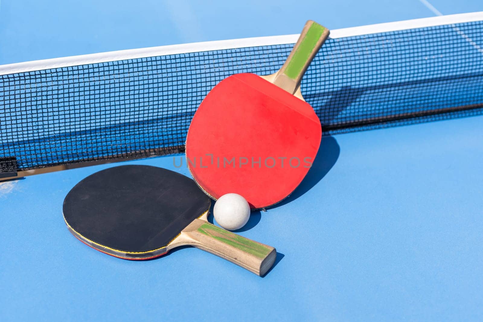 Two table tennis or ping pong rackets and ball on blue table with net. High quality photo